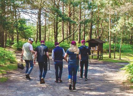 An image of a group of people walking in the woods, Clay Pigeon Shooting Near London. Bisley Shooting Ground
