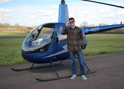 An image of Helicopter R22 and a man standing before his flight