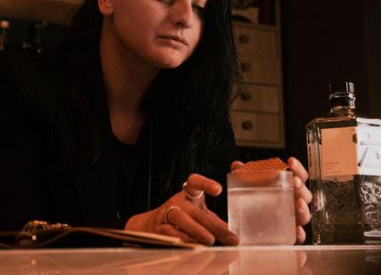 A woman prepares a drink at a bar, holding a glass with a large ice cube 