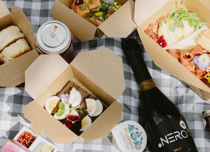 An image of a bottle of wine and food on a picnic blanket