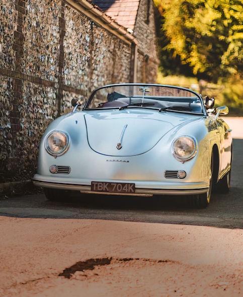 An old porsche speedster parked in front of a brick wall.