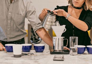 An image of a man and woman pouring coffee, Home Brew Master Class. The Artisan Coffee School