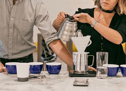 An image of a man and woman pouring coffee, Home Brew Master Class. The Artisan Coffee School