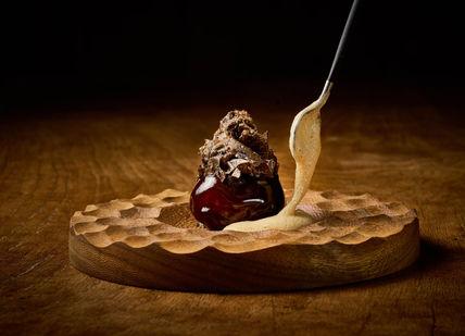 A spoon is being dipped in chocolate on a wooden plate.