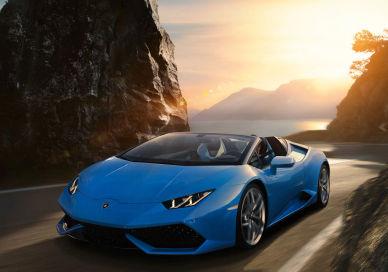 An image of a blue lamb car driving down a mountain road, One day hire of Lamborghini Huracan or Ferrari 488 Spider. Edel & Stark