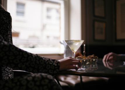 An image of a woman sitting at a table with a martini, Martini Masterclass. The Egerton House Hotel