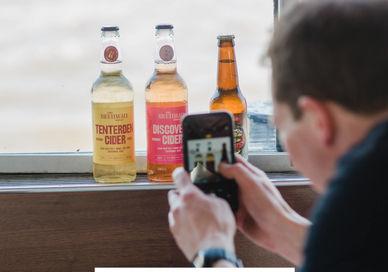 An image of a man taking a picture of a bottle of beer, Two Exclusive Tickets to a London Craft Cider Cruise on The Thames. James Kellow (Crafty Bar Stars)