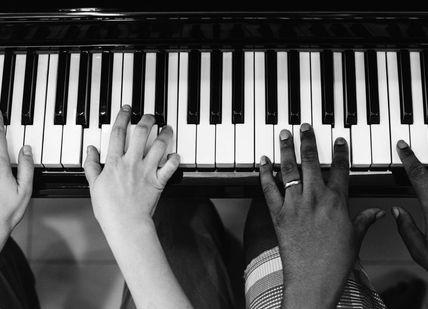 An image of two people playing the piano, Private Piano Lesson. The London Piano Institute