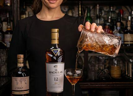 An image of a woman pouring a drink, Macallan Whisky Experience with Cheese Pairing and Tapas. Map Maison
