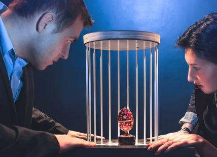 An image of a man and woman looking at a small red heart in a cage, Capital Caper Escape Room Adventure. Mazer Zone