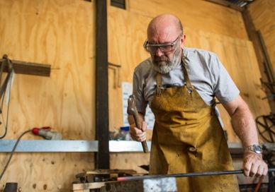 An image of a man working on a piece of wood, Blacksmithing Taster Experience. Now Strike Archery