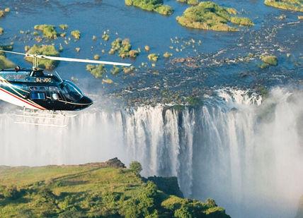 An image of a helicopter flying over a waterfall, Pretoria to Victoria Falls by Train. Rovos Rail