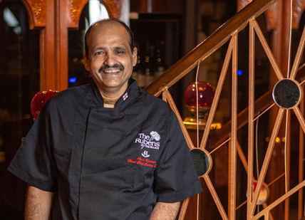 An image of a man that is standing in front of a table, Gourmet Experience with Chef Kumar. The Rubens at the Palace - The Curry Room
