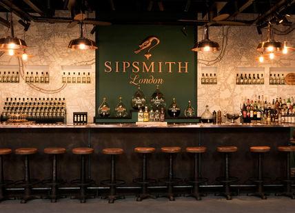 An image of a bar with stools and a wall of wine bottles, Sipsmith Distillery. Sipsmith Distillery