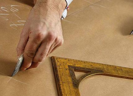 An image of a person cutting a piece of cardboard, Create a Bespoke Two-Piece Suit. Stowers London