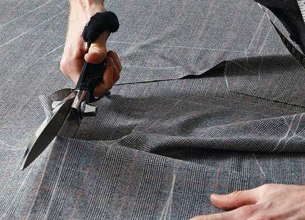 An image of a man cutting a piece of fabric, Create a Bespoke Two-Piece Suit. Stowers London