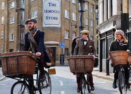 An image of two people riding bicycles down the street, Bike Ride and Gin Tour. Tally Ho