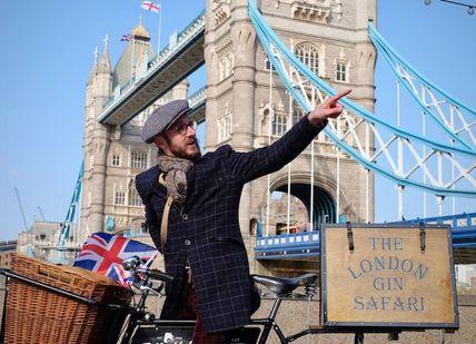 An image of a man on a bike with a sign, Bike Ride and Gin Tour. Tally Ho