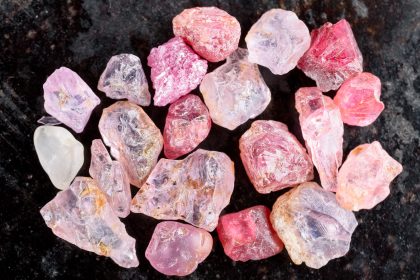 Collection of pink and red rough uncut spinel gemstones on black stone slate.