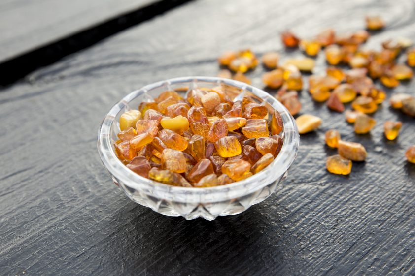 Cute little bowl cup full of small Baltic amber chips on dark brown wooden background. The Baltic region is home to the largest known deposit of amber, called Baltic amber or succinite.