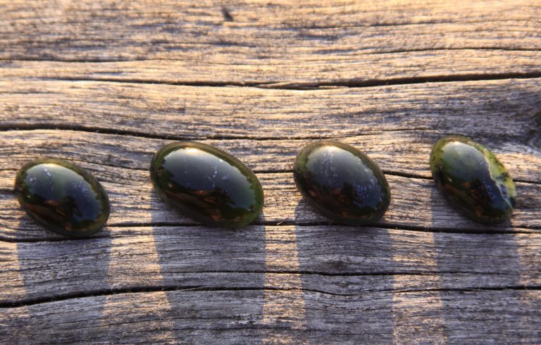 Black jade translucent green stone in sunlight on wood. The black jade is dark green in color, but under the light it is semi-transparent, appreciated by jewelers because the way it shines