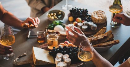 Group of people drinking orange or rose wine, eating various gourmet snacks cheese grape bread for company over concrete table background. Gathering, celebrating, wine tasting concept