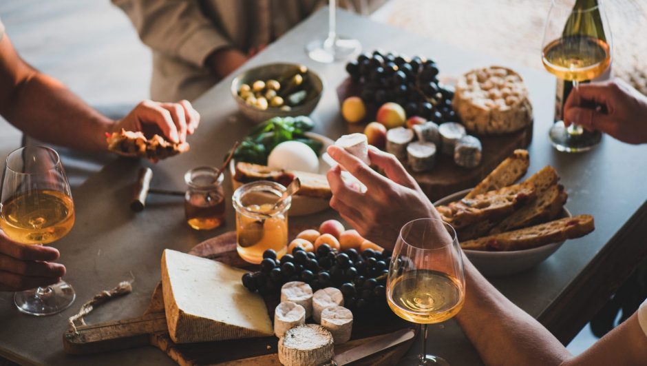 Group of people drinking orange or rose wine, eating various gourmet snacks cheese grape bread for company over concrete table background. Gathering, celebrating, wine tasting concept