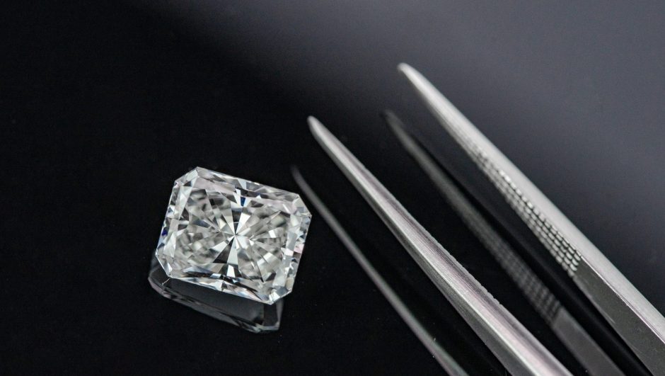 Radiant cut diamond with tweezers on black reflection background