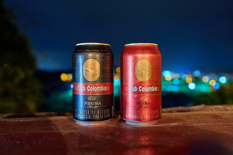 Guatape, Colombia - Circa 2019: Cans of Club Colombia beer on a counter with view over the resort town at night. Red and Black versions
