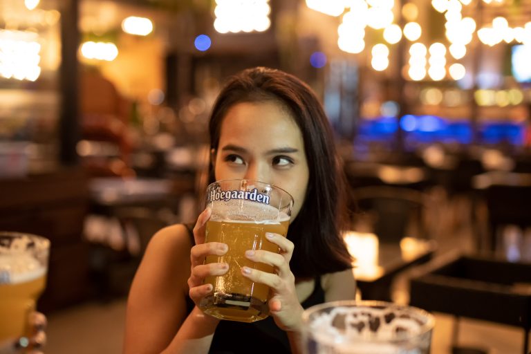 Udon Thani, Thailand - Oct 21, 2018: Hoegaarden beer glass cheers on beautiful girl friends on Friday night party at restaurant bar in new years, blur bokeh background.Girl holding glass of beer.