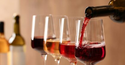 Pouring wine from bottle into glass on blurred background, closeup